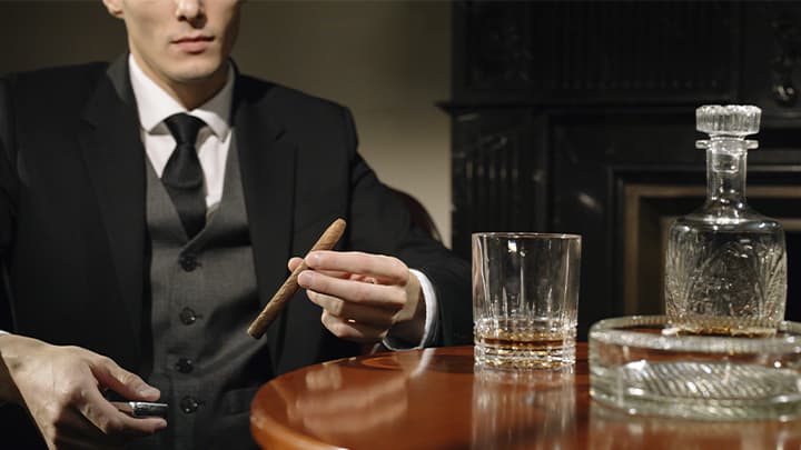 Man holds cigar and glass on table